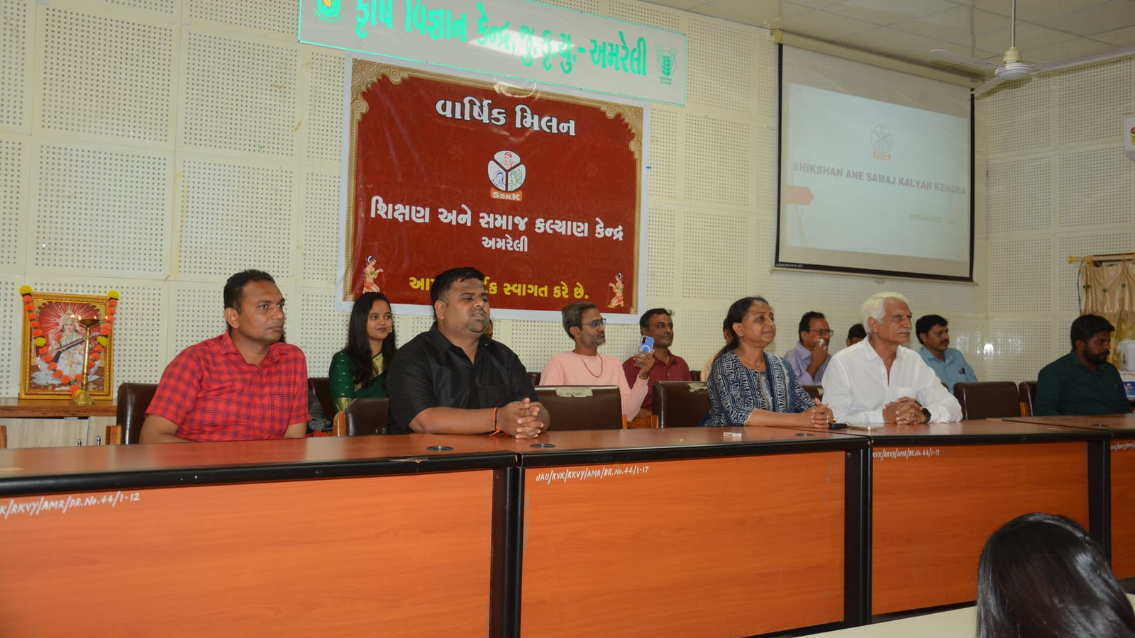 અમરેલીમાં SSKKના વાર્ષિક મિલનમાં ટેબલ પાસે બેઠેલા સભ્યો, પાછળ સંસ્થાનું બેનર