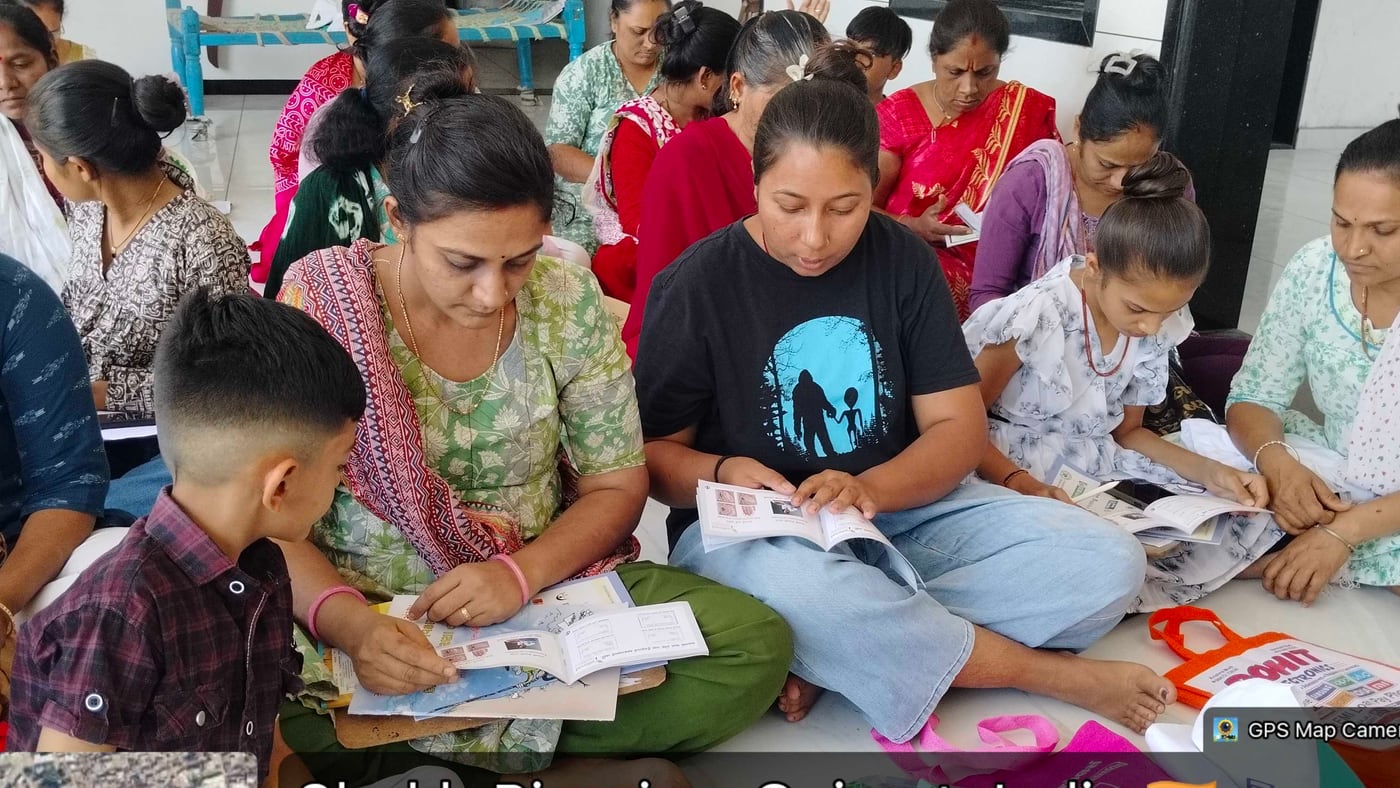Women sitting on the floor at a camp, filling in printed forms, some helping each other read them