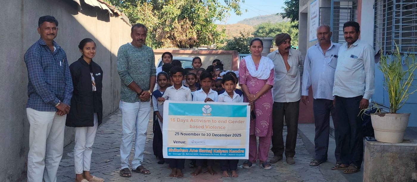 Staff, villagers and schoolchildren standing outside a village school holding a printed banner reading “16 Days Activism to end Gender based Violence, 25 November to 10 December 2025”